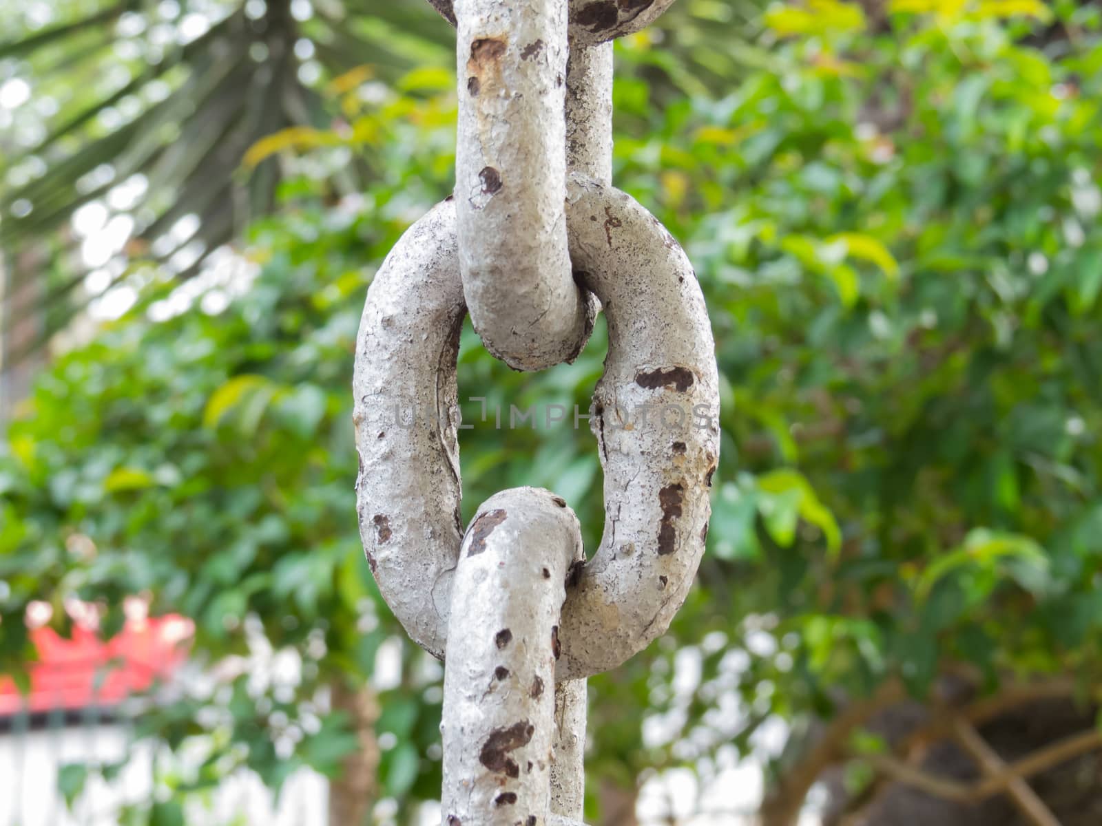 Close up of rusty chain links in foreground, with green on background