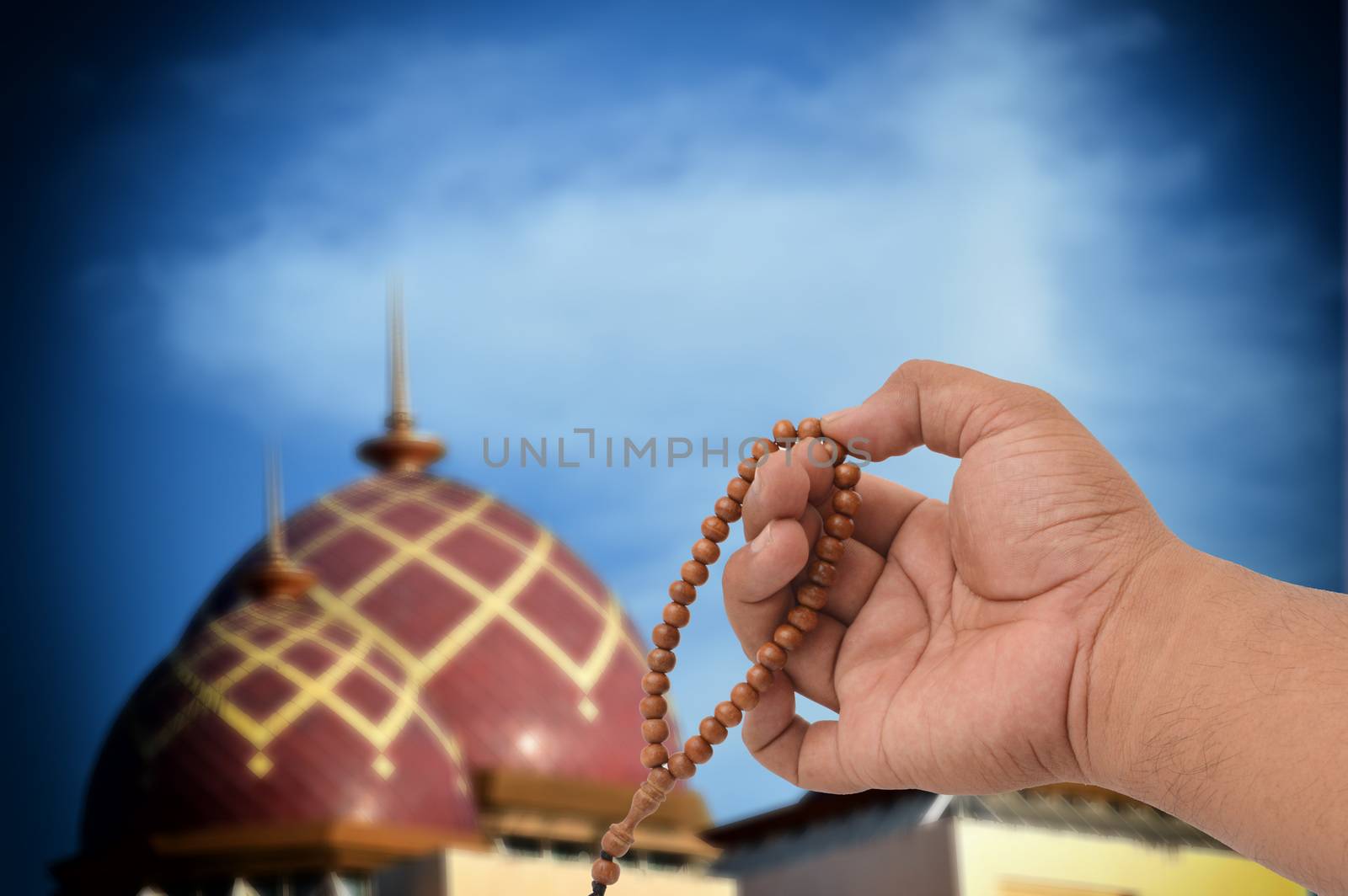 Muslim male hands holding rosary with mosque blurry background