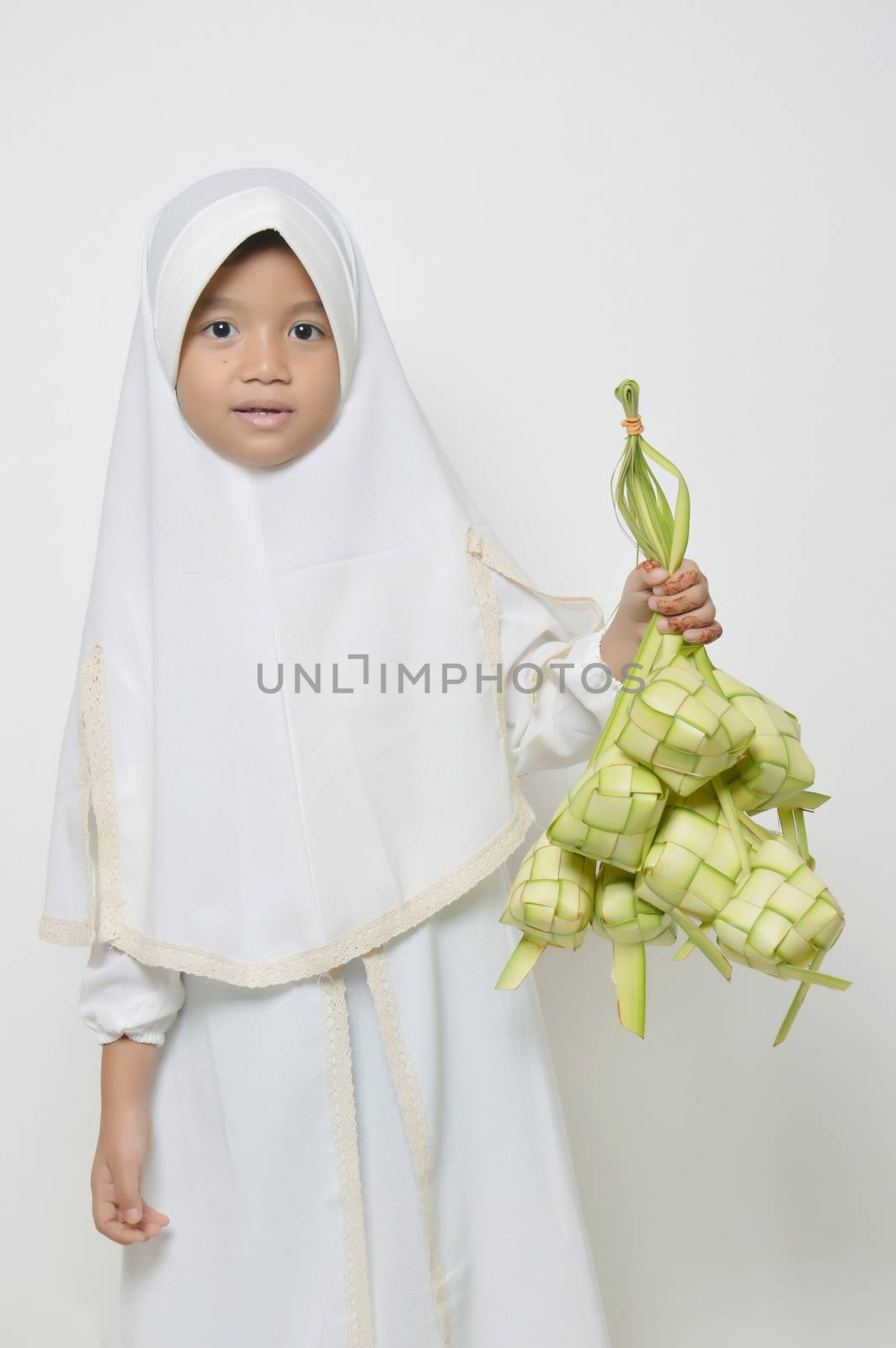 Moslem Asian little girl dressed with hijab in white holds ketupat
