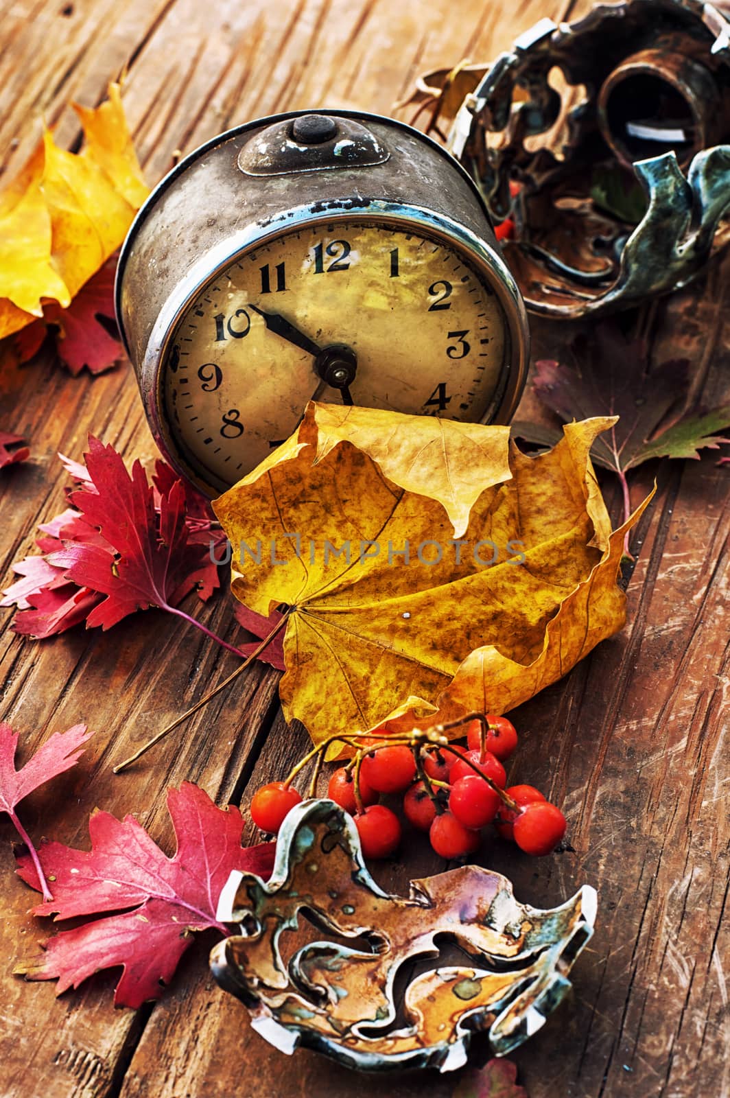 Autumn still life with an alarm clock and fallen leaves.