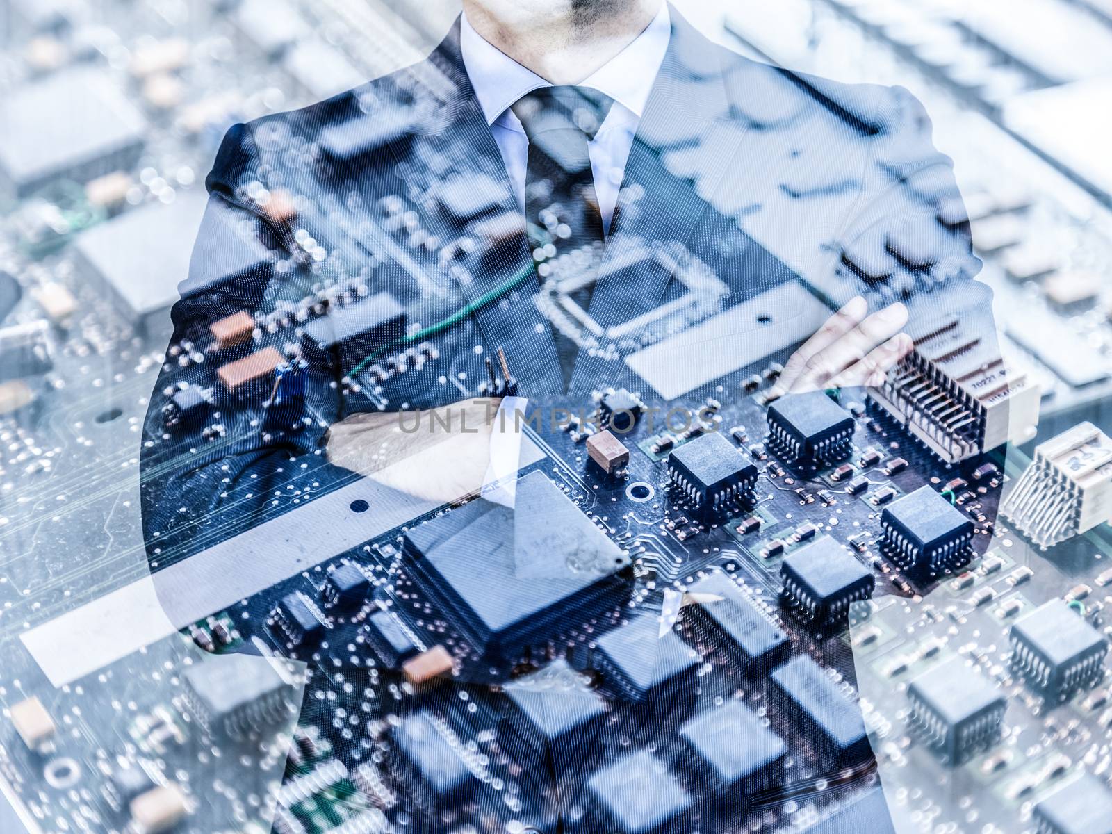 Torso of a businessman standing with folded arms in a classic navy blue suit against pc motherboard chip photo layer.