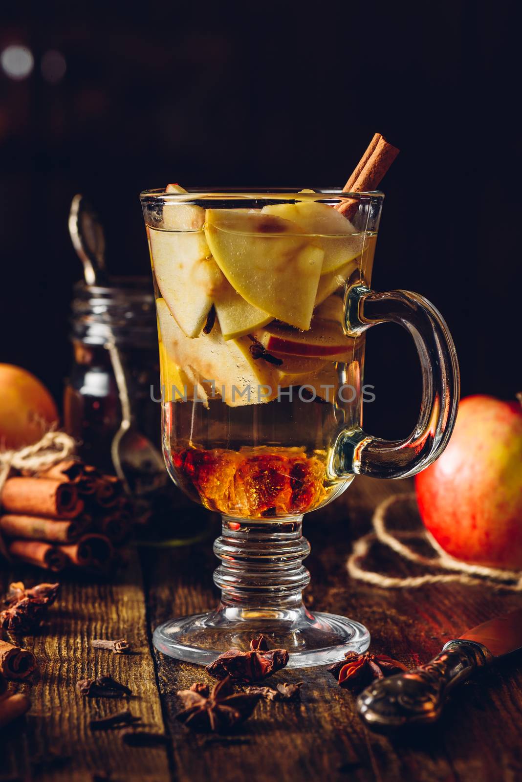 Glass of Apple Mulled Drink with Clove, Cinnamon, Anise Star and Dark Candy Sugar. All Ingredients and Some Kitchen utensils on Wooden Table. Vertical.