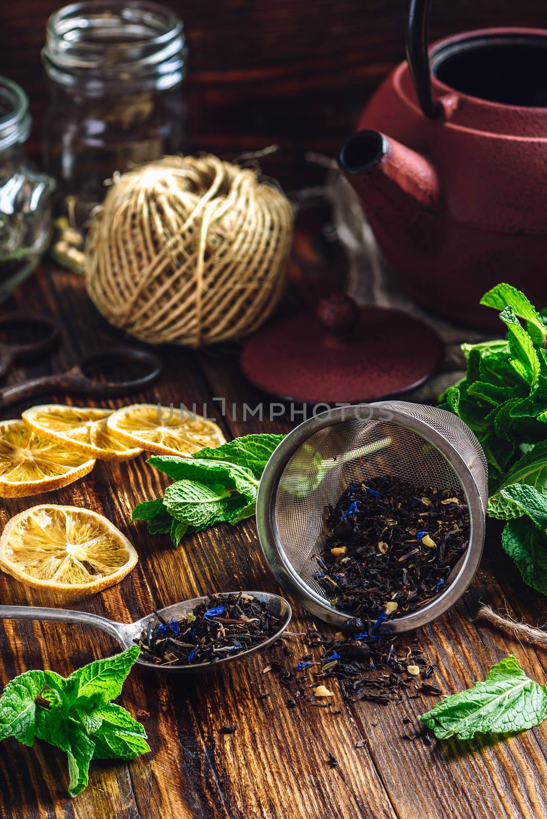 Dry Tea in Strainer and Spoon with Fresh Mint and Lemon Slices. Tangle with Two Jars and Teapot on Backdrop.