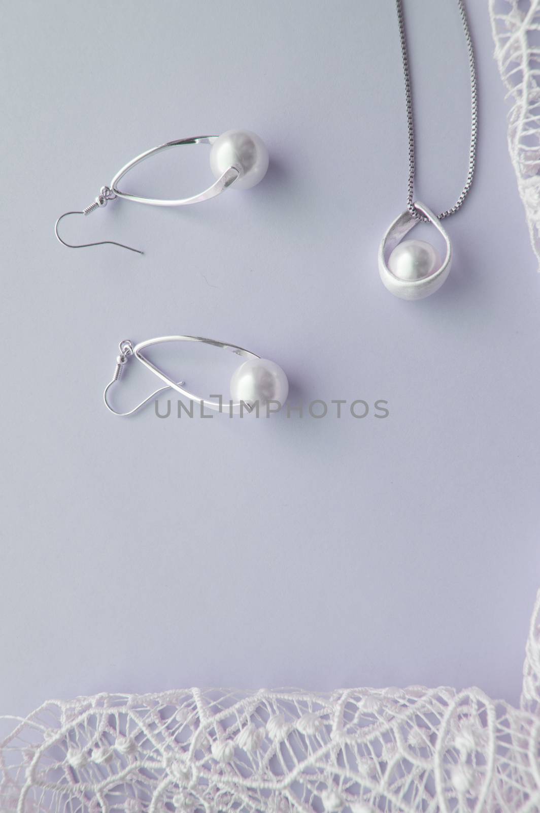 Beautiful silver shiny pearl jewelry, trendy glamorous earrings, chain on delicate pastel background with exquisite lace. Lay flat, top vertical frame by claire_lucia