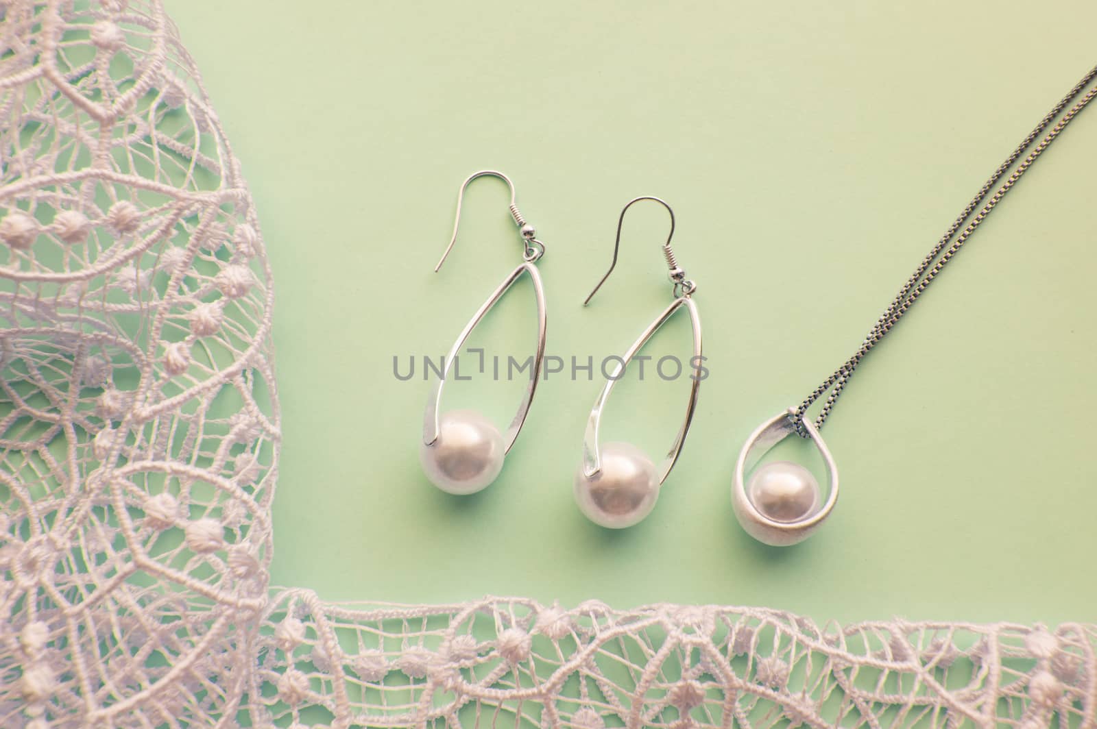 Fashion women's silver accessories - earrings and pendant with pearls on light background with rich openwork lace, top view, flat, space for text.