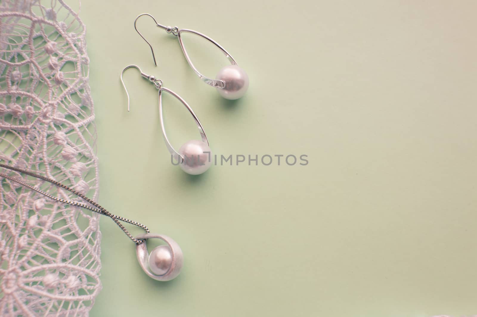 Fashion women's silver accessories - earrings and pendant with pearls on light background with rich openwork lace, top view, flat, space for text.