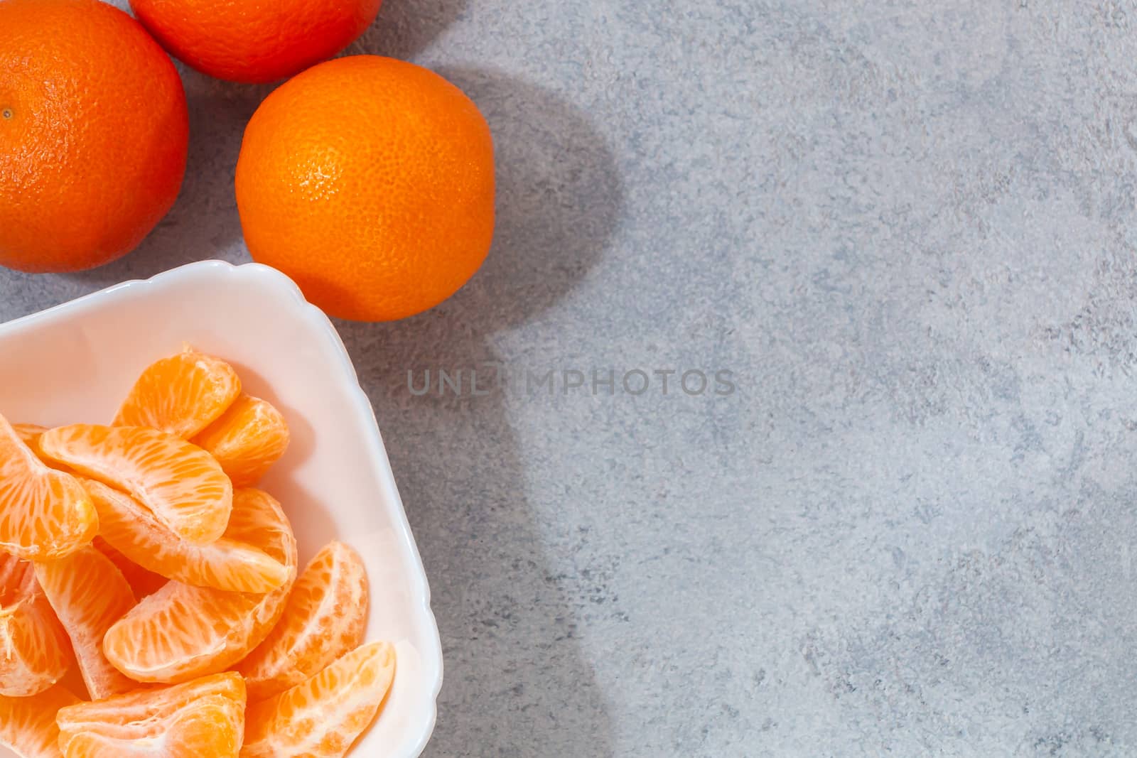 Several whole and peeled ripe tangerines on a white plate on gray background with space for text, flat lay, top view by galsand