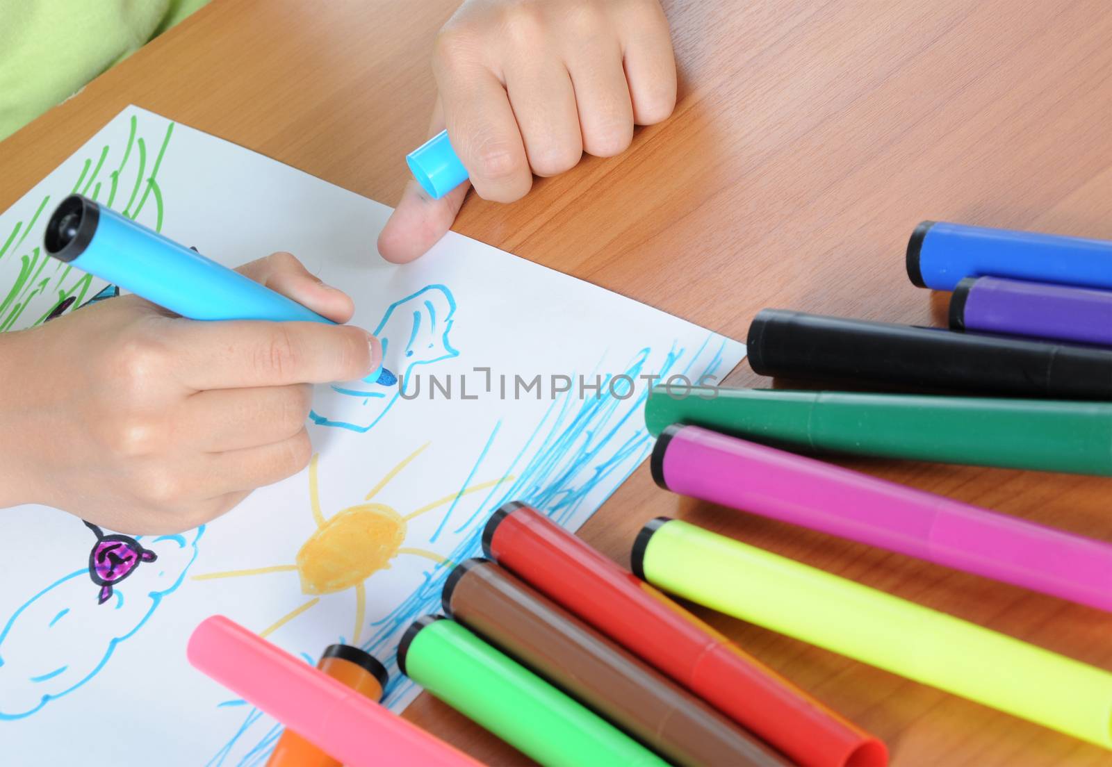 Unrecognizable child drawing picture on paper by colours pencil