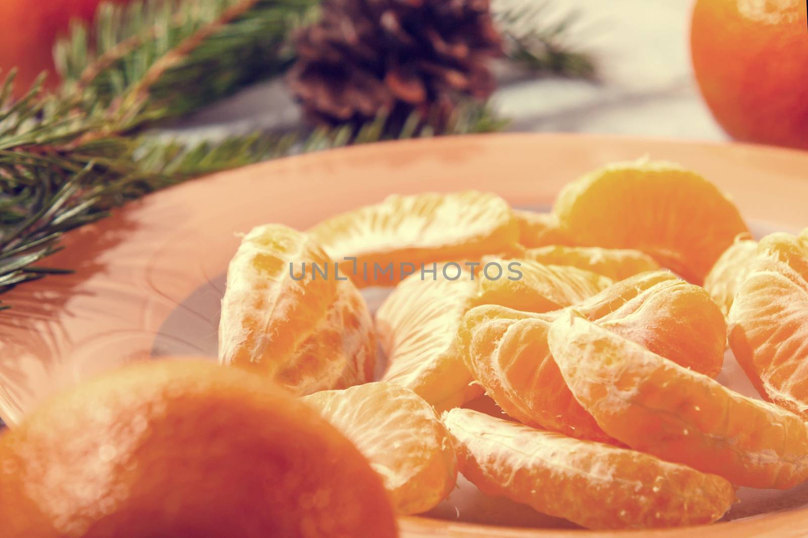 Several peeled tangerine slices on an orange plate with tree branches and a cone-a traditional Christmas and new year's composition in Russia by galsand