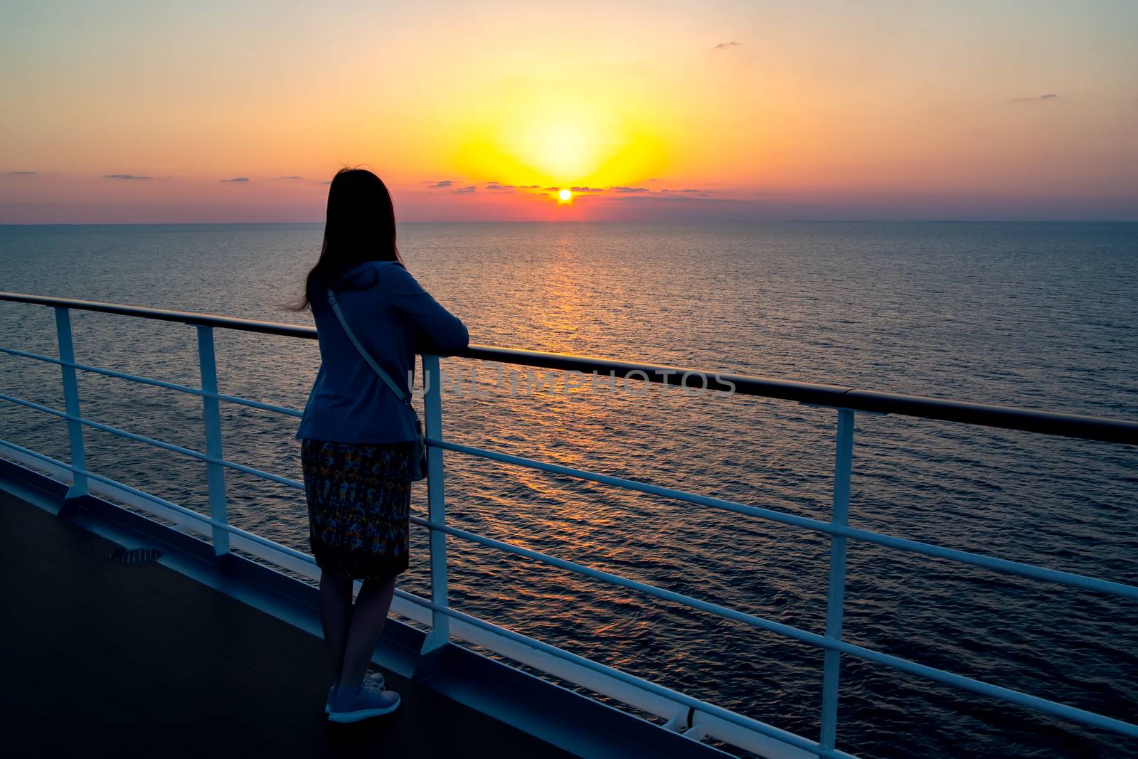 young girl admires the sunset on the sea standing aboard a cruise liner.
