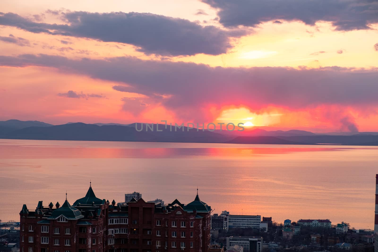 View of the city of Vladivostok from the hill eagle's nest . Sunset. The sky is orange and pink. Sea and city at sunset.