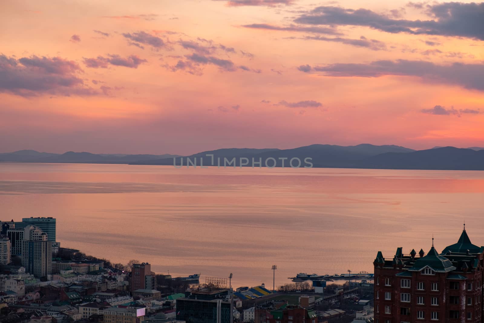 View of the city of Vladivostok from the hill eagle's nest . Sunset. The sky is orange and pink. Sea and city at sunset.