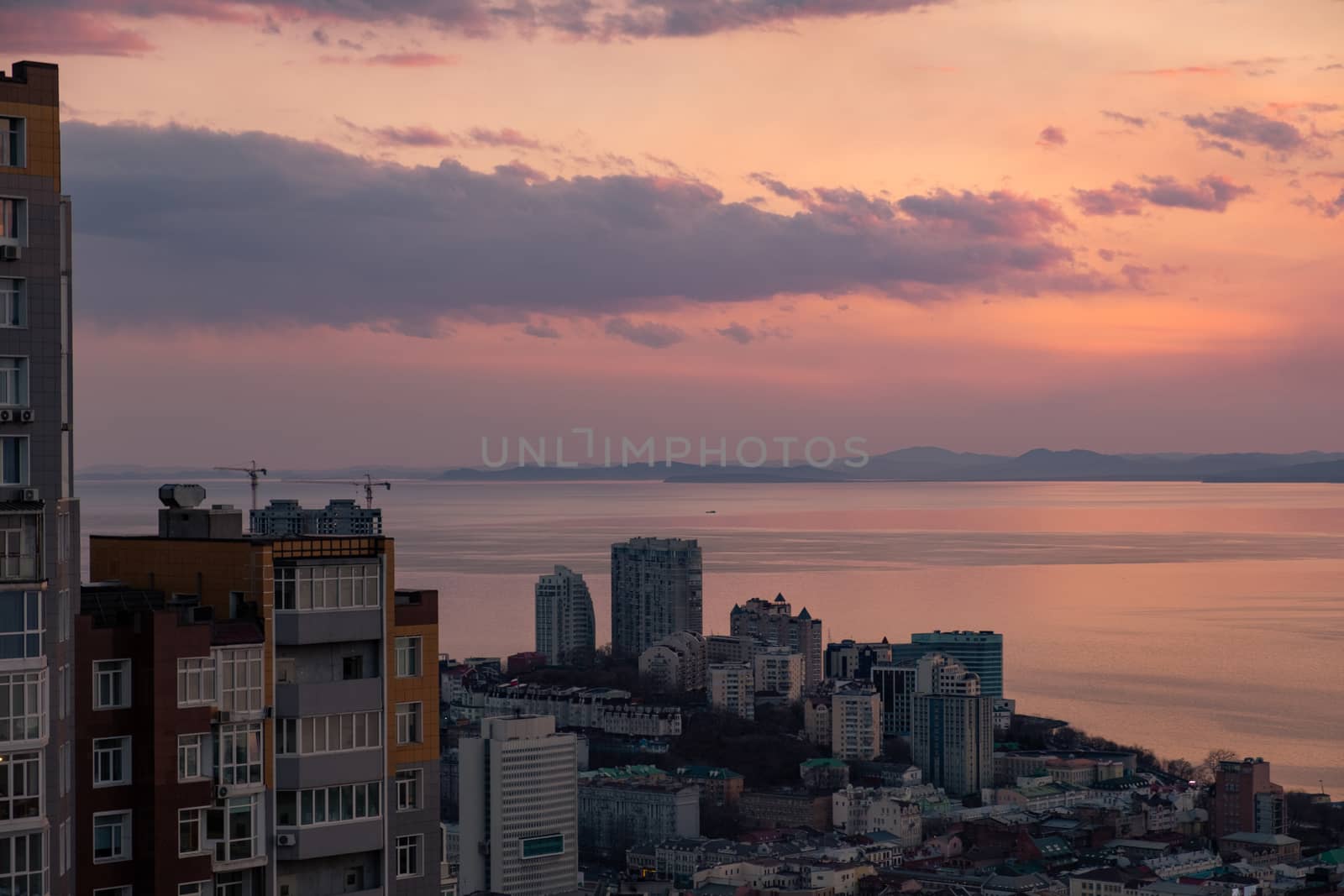 View of the city of Vladivostok from the hill eagle's nest . Sunset. The sky is orange and pink. Sea and city at sunset.