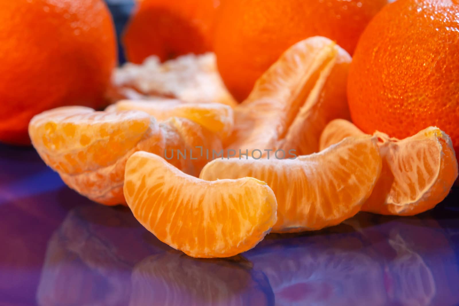 Several whole and peeled ripe tangerines on a blue plate.