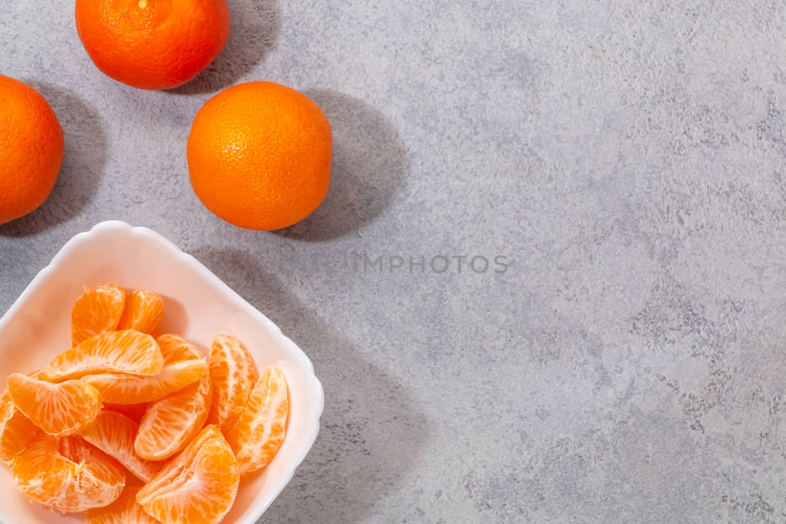 Several whole and peeled ripe tangerines on a white plate on gray background with space for text, flat lay, top view by galsand