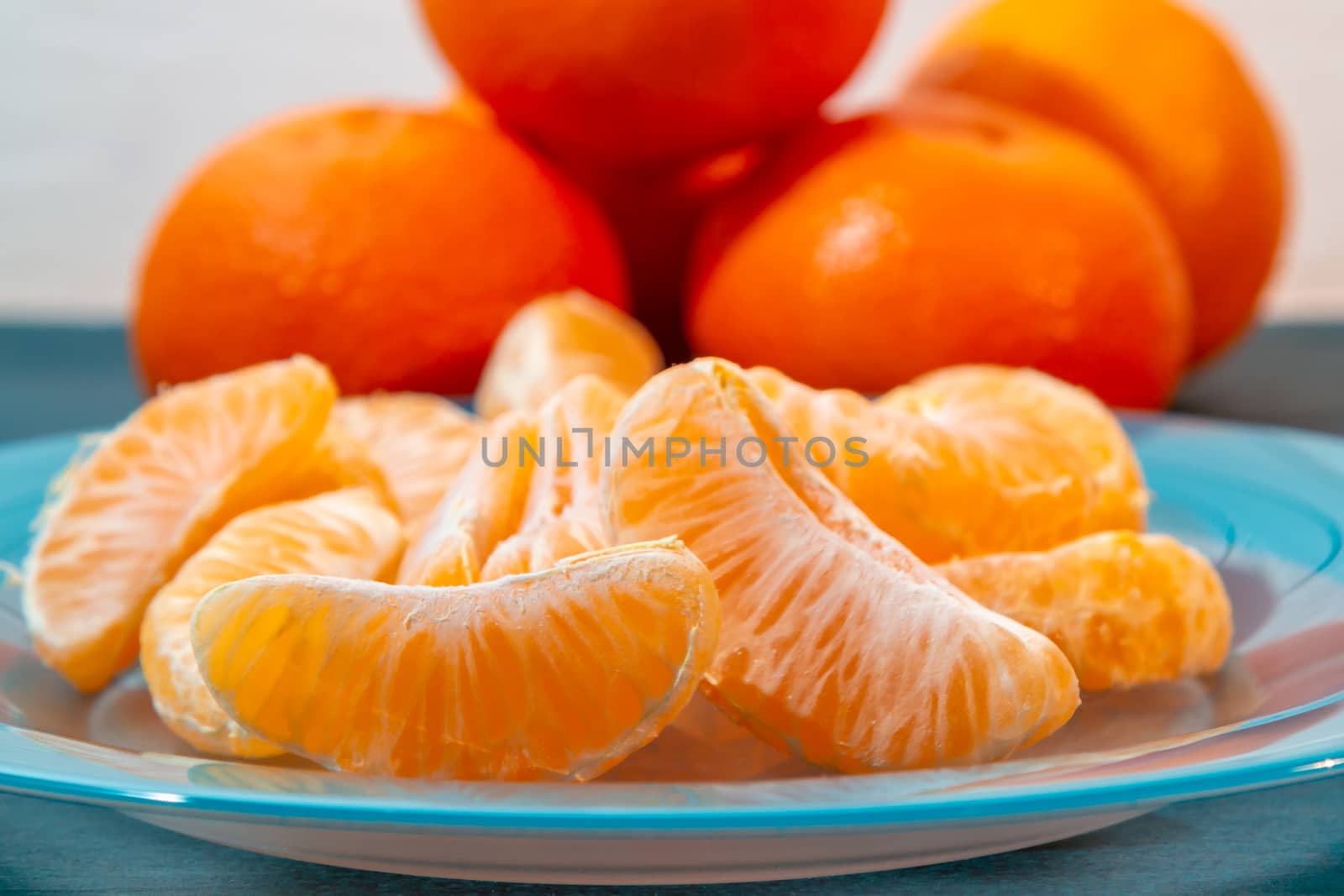 Several whole and peeled ripe tangerines on a turquoise plate by galsand