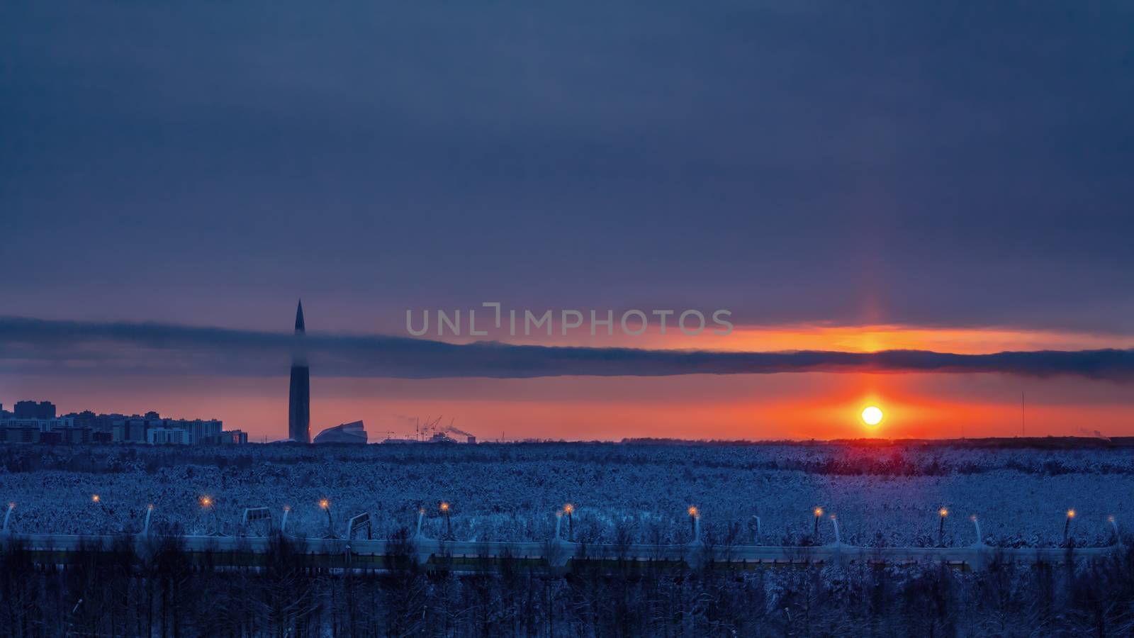 Colorful sunset in the cloudy sky over a snowy forest on the outskirts of the city.