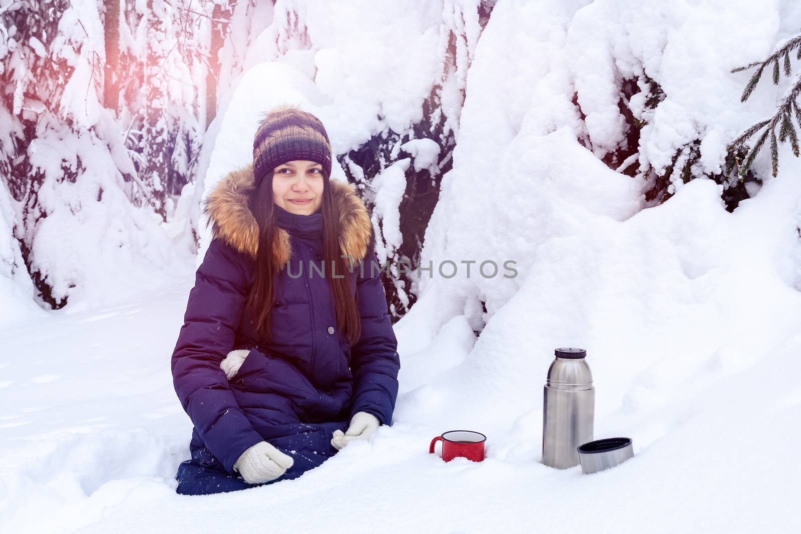 girl drinks coffee from a thermos while walking through a snowy winter forest.