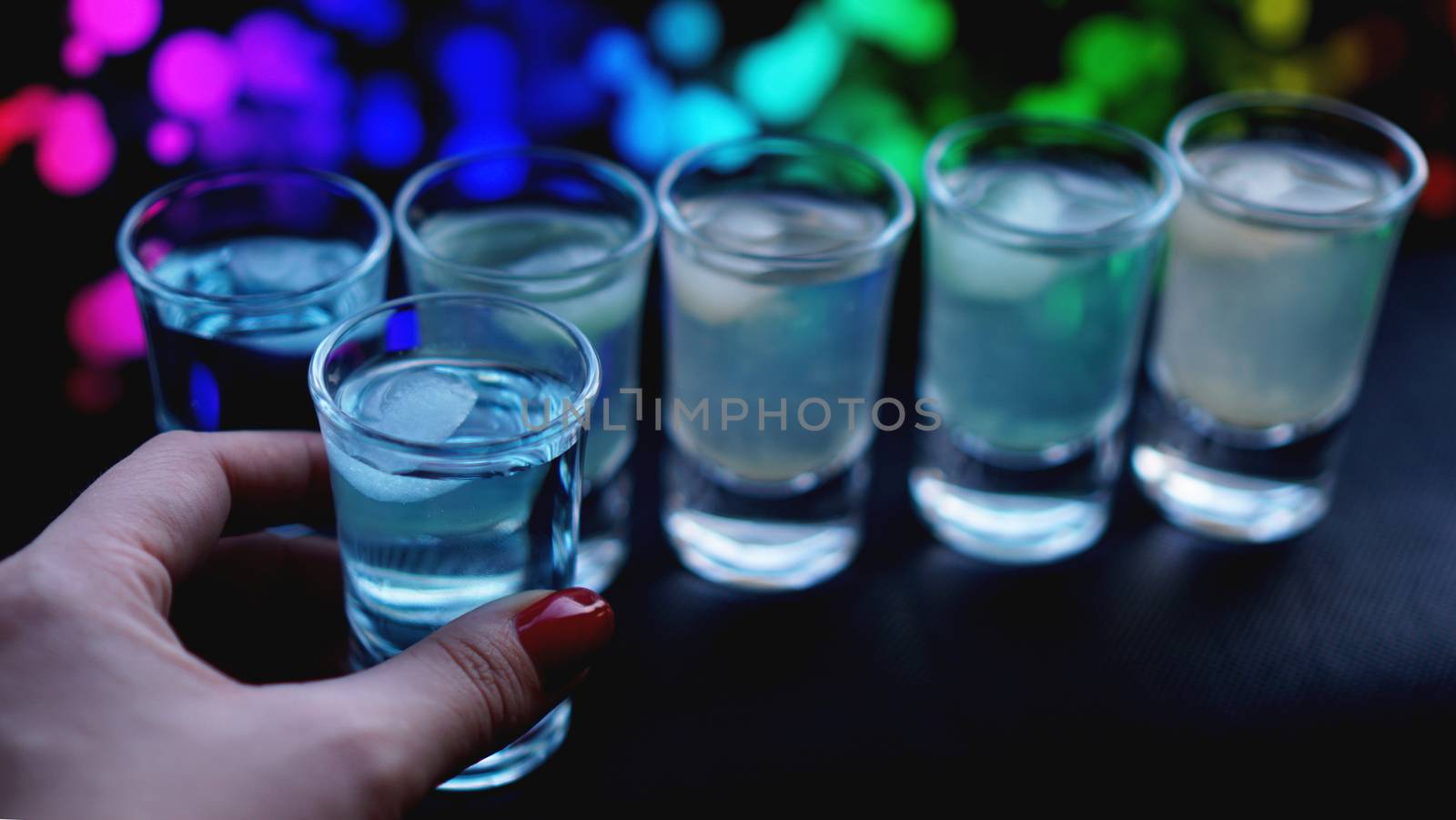 Female hand with a shot of alcohol, neon blurred background in bar