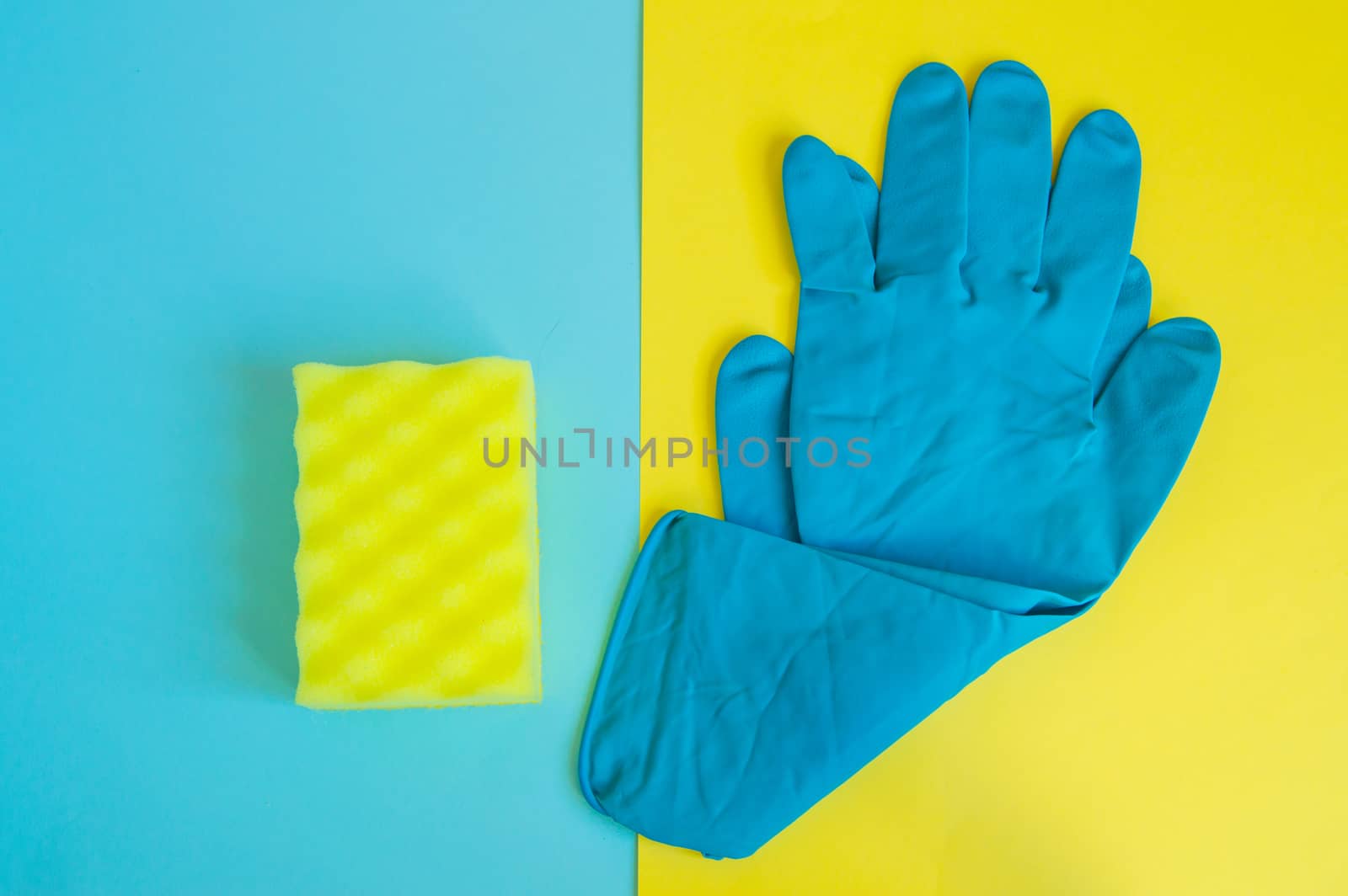 Professional concept of cleaning the house, accessories for a spring cleaning, blue rubber gloves and cleaning sponge on a double yellow and blue background, flat lay.