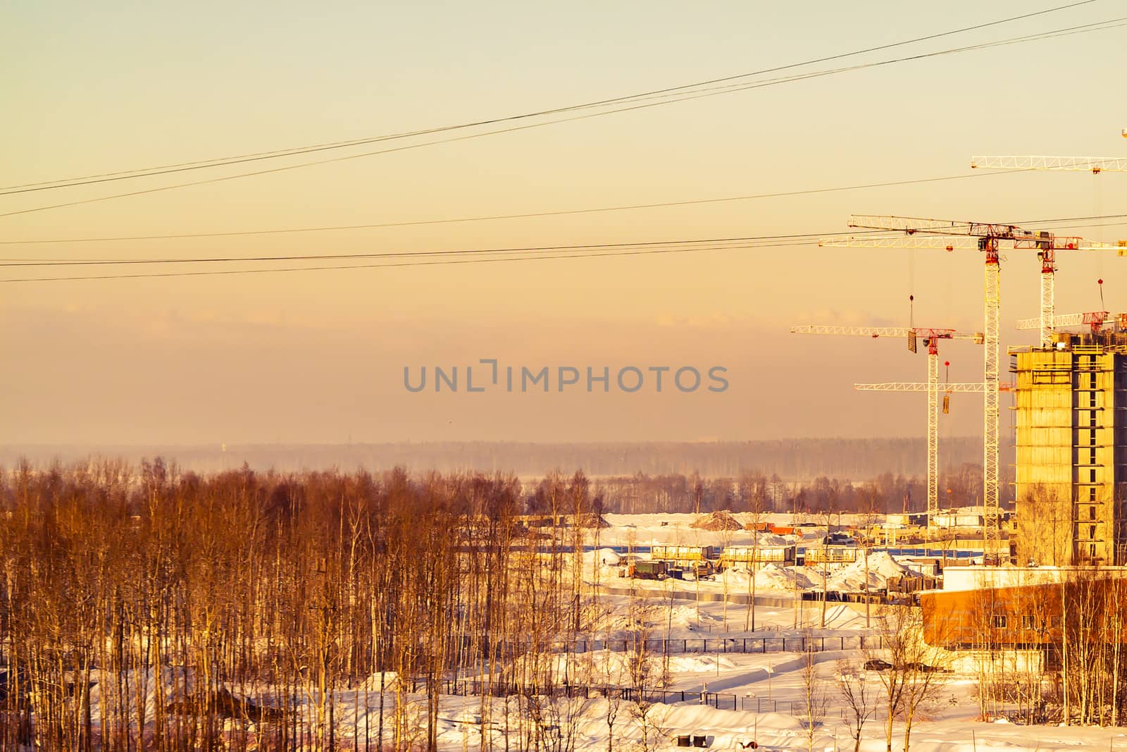 Construction on the outskirts of the city - construction equipment, cranes, started houses, surrounded by fields and cut down forests.