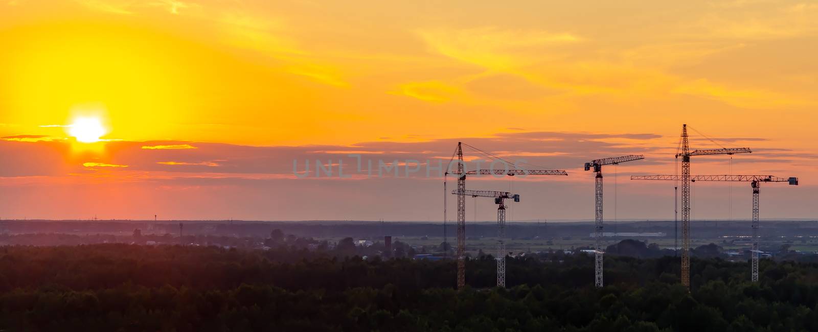 Several construction cranes on the background of colorful sunset sky.