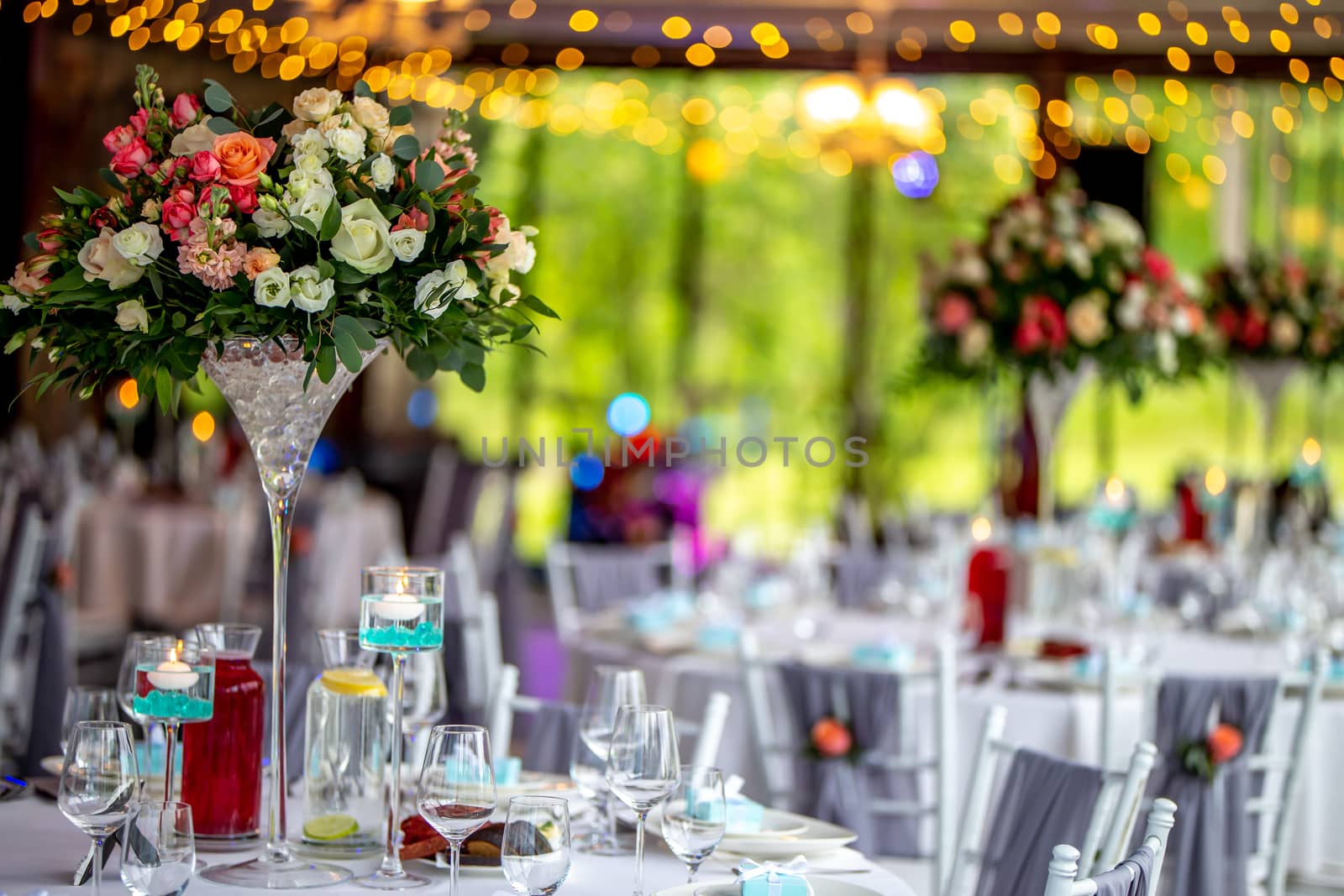 Wedding table decoration. Beautiful bouquet of flowers in vase on the table, next to plates,  glasses and gift boxes. Bouquet of flowers, glasses, gift boxes and jugs setting on the festive table in restaurant.