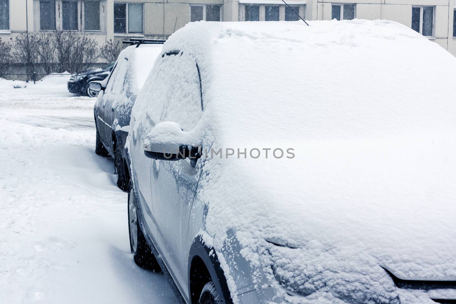 Snowfall in the city, cars overwhelmed with snow.