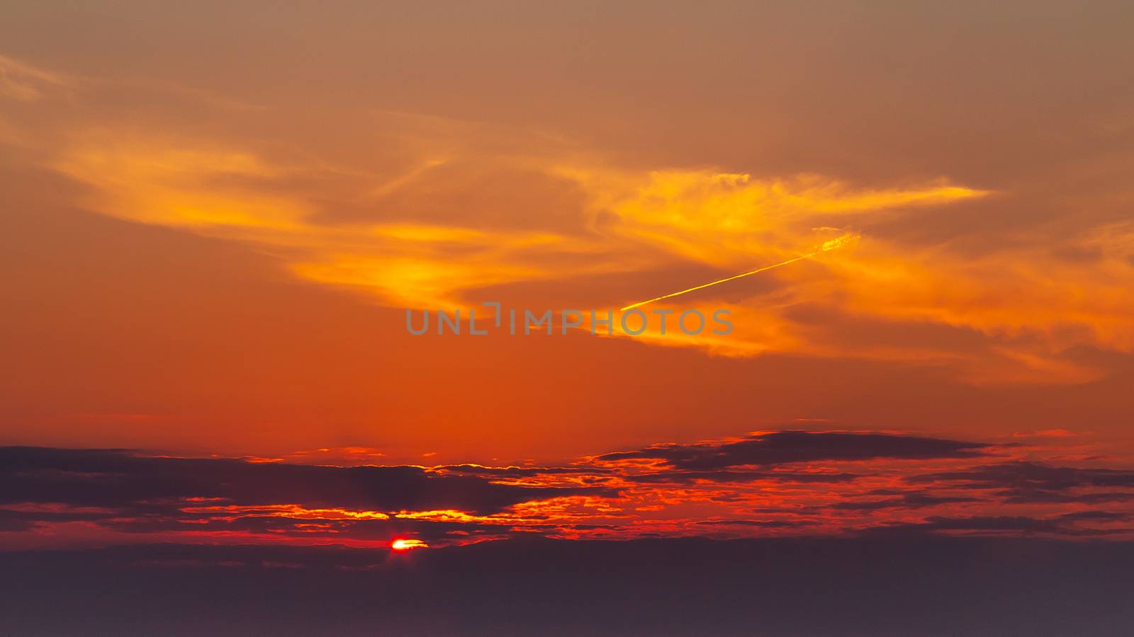 sky during a colorful, bright orange sunset, sun's rays make their way through the clouds.