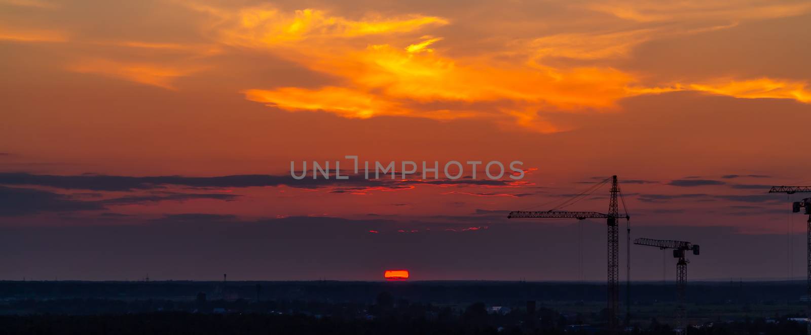 Several construction cranes on the background of colorful sunset sky.