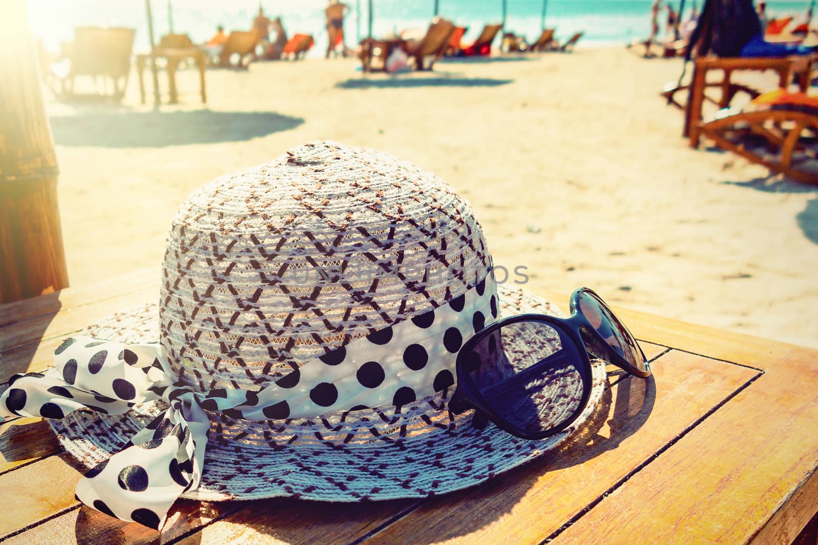 Women's hat and sunglasses lie on a wooden table on a sunny sandy beach by the sea by galsand