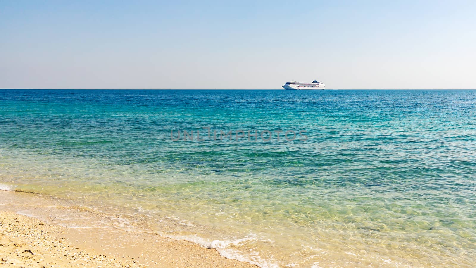 Turquoise sea with light ripples on the water and a large cruise liner on the horizon.