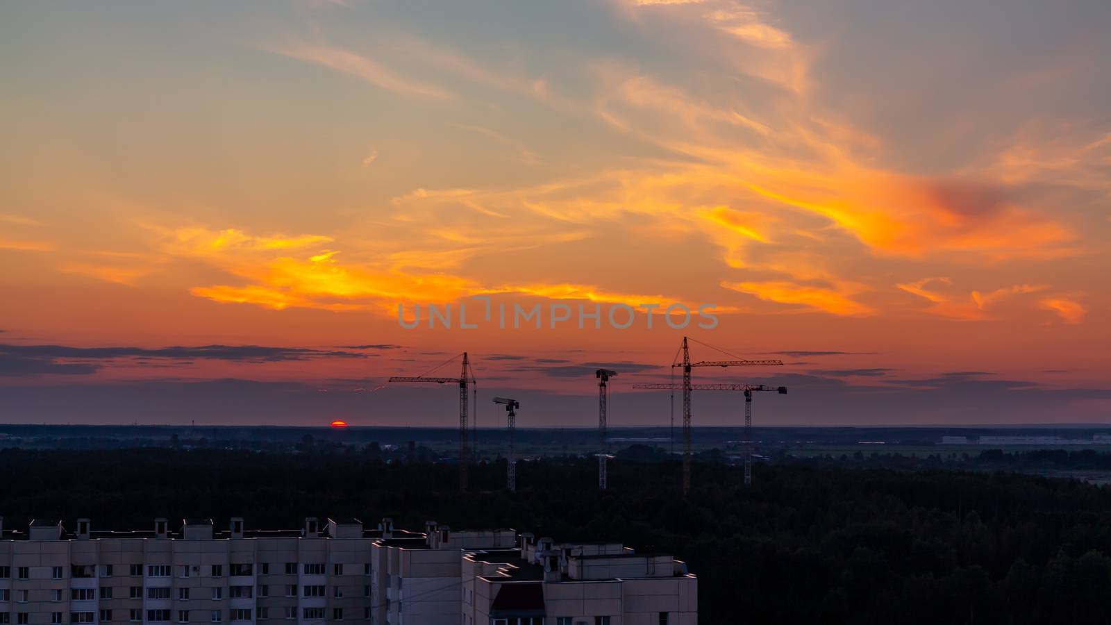 Several construction cranes on the background of colorful sunset sky.