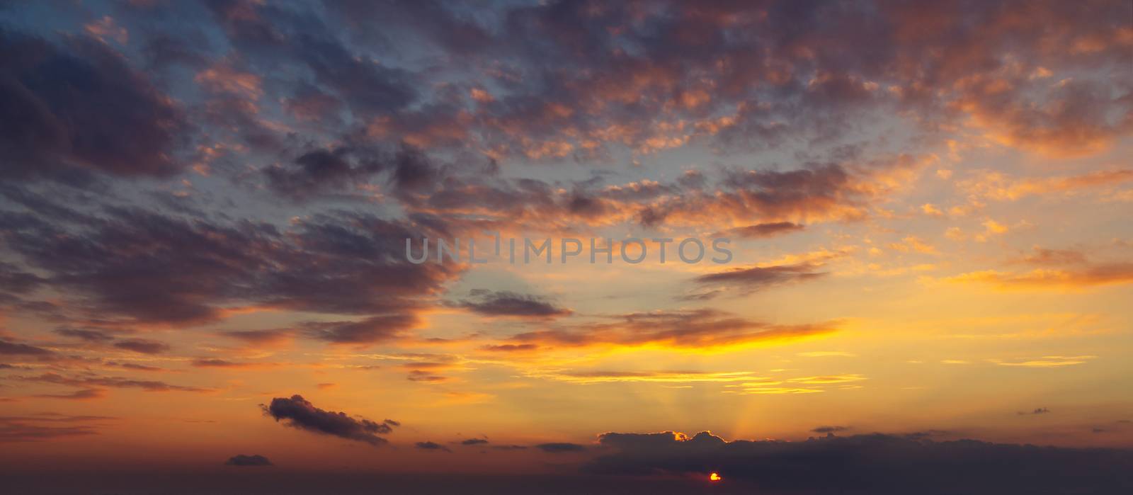 sky during a colorful, bright orange sunset, sun's rays make their way through the clouds by galsand