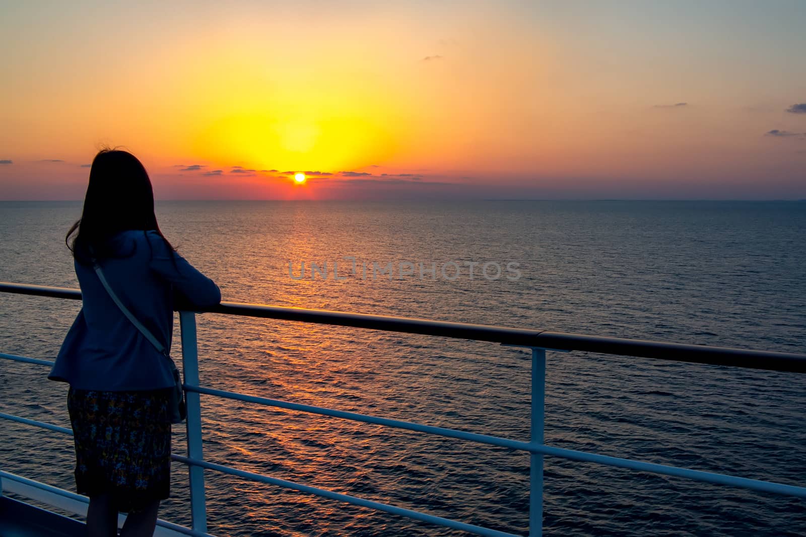 young girl admires the sunset on the sea standing aboard a cruise liner.