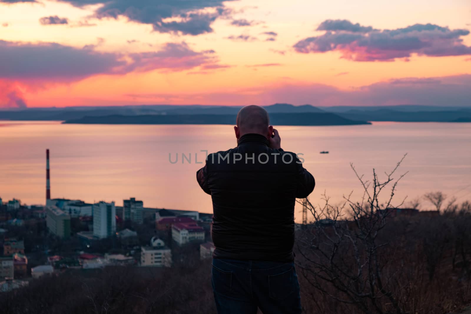 A man photographs a panoramic view of the city of Vladivostok during sunset. City view from above. The sea on the horizon. by rdv27