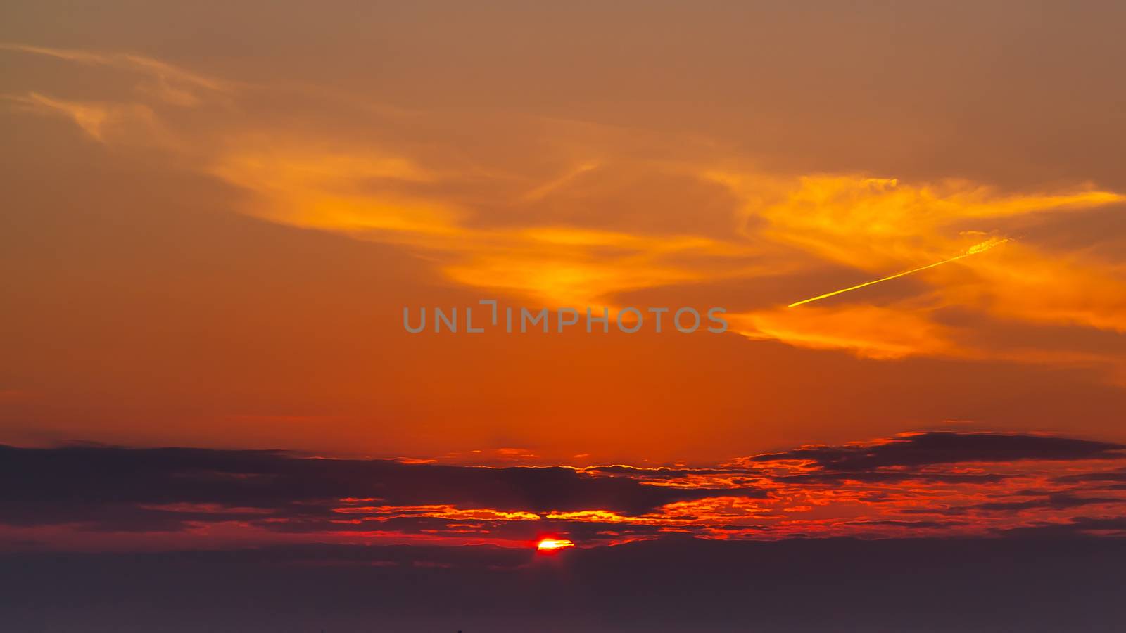 sky during a colorful, bright orange sunset, sun's rays make their way through the clouds.