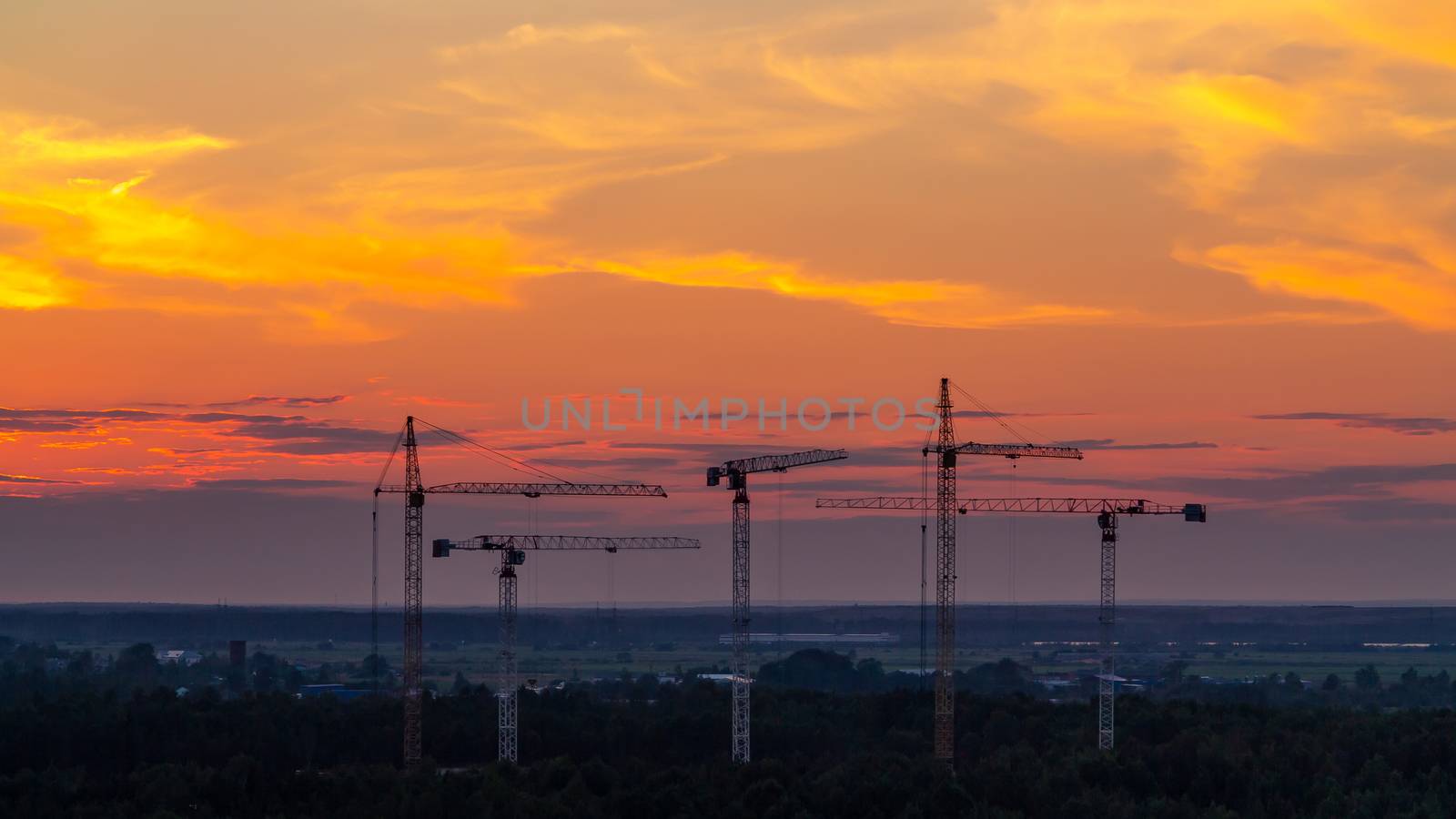 Several construction cranes on the background of colorful sunset sky.