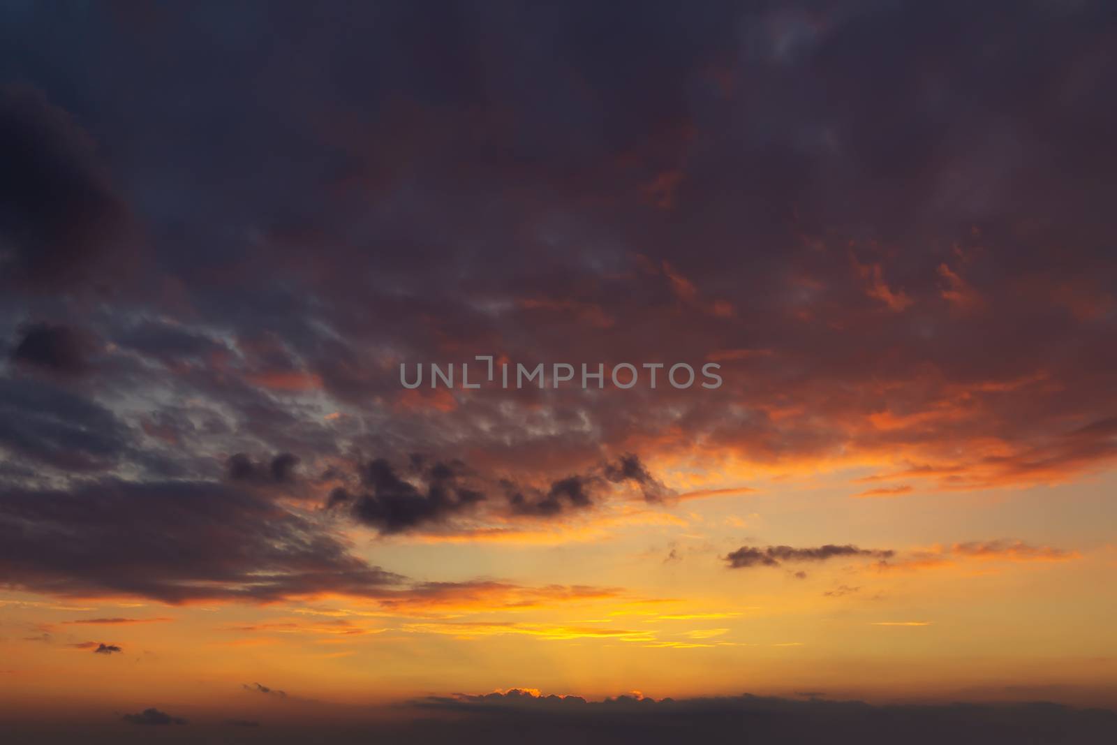 sky during a colorful, bright orange sunset, sun's rays make their way through the clouds.