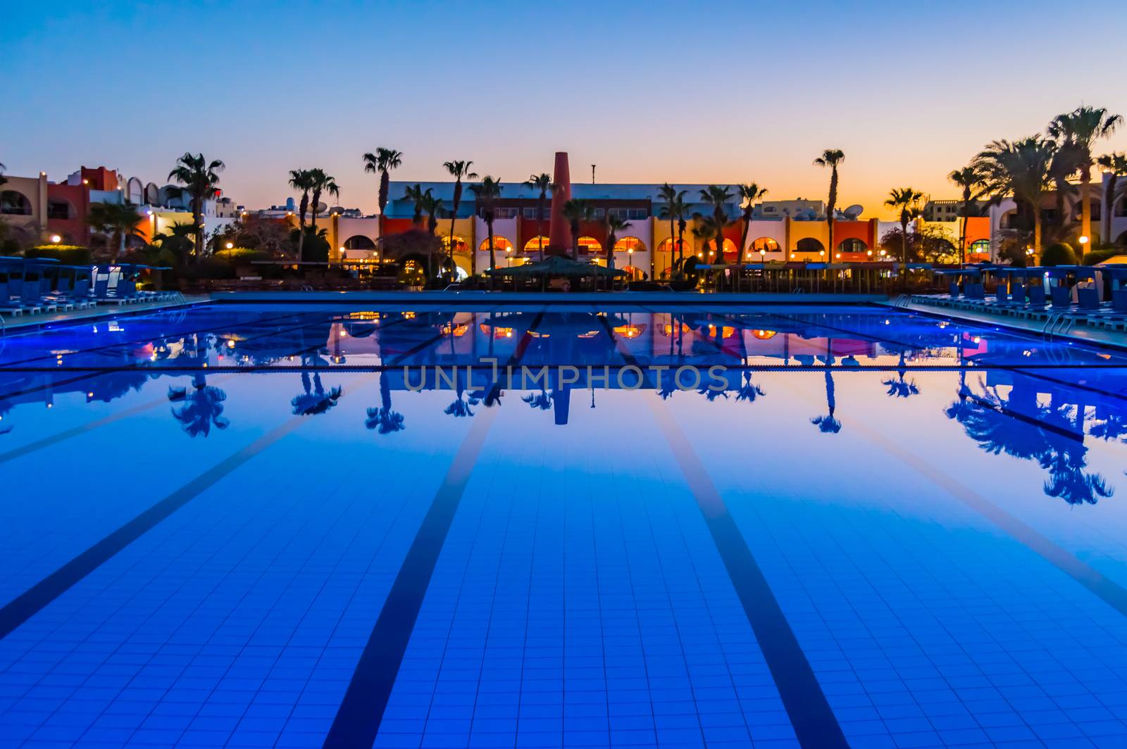 View of a pool at sunset with reflections of palm trees  by Philou1000
