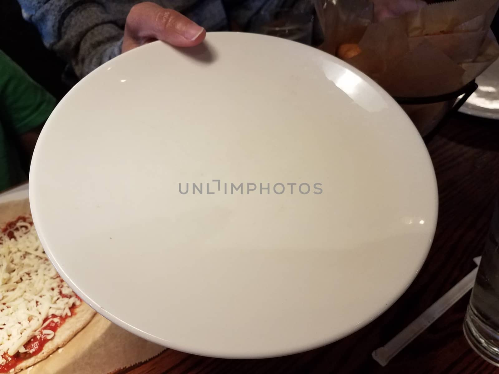 woman's hand holding a large white plate and pizza