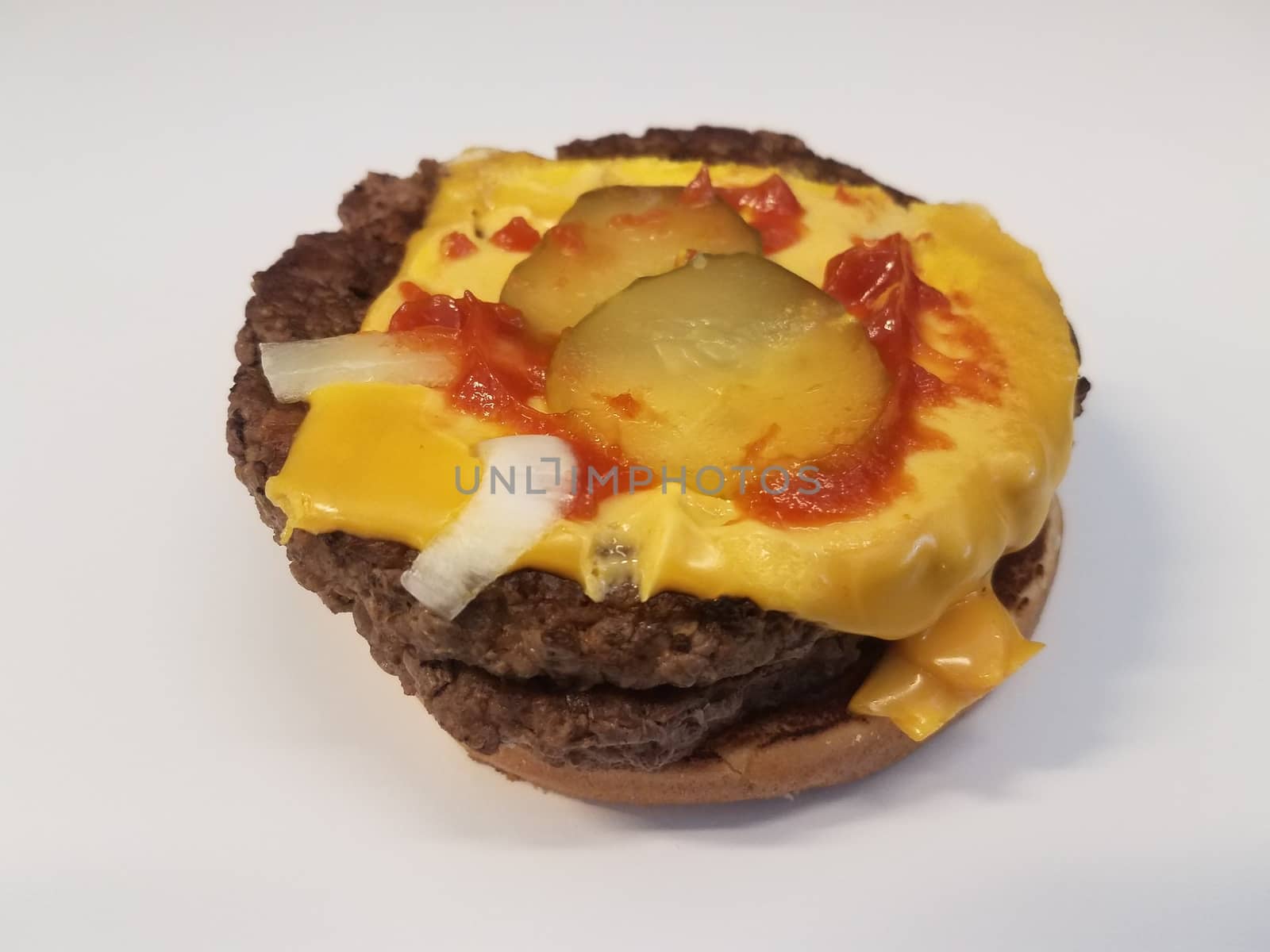 hamburger with cheese and pickles and ketchup and onions on white surface