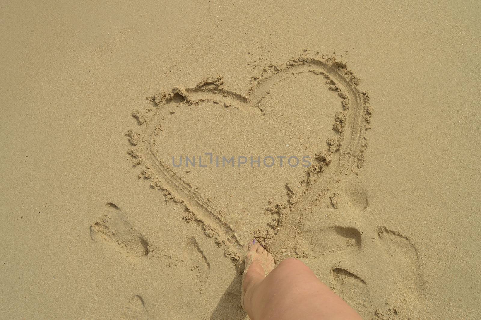 Hello summer, women's feet draw a heart sign on the wet sand while standing on the sandy beach. Concept of rest, relaxation, top view by claire_lucia