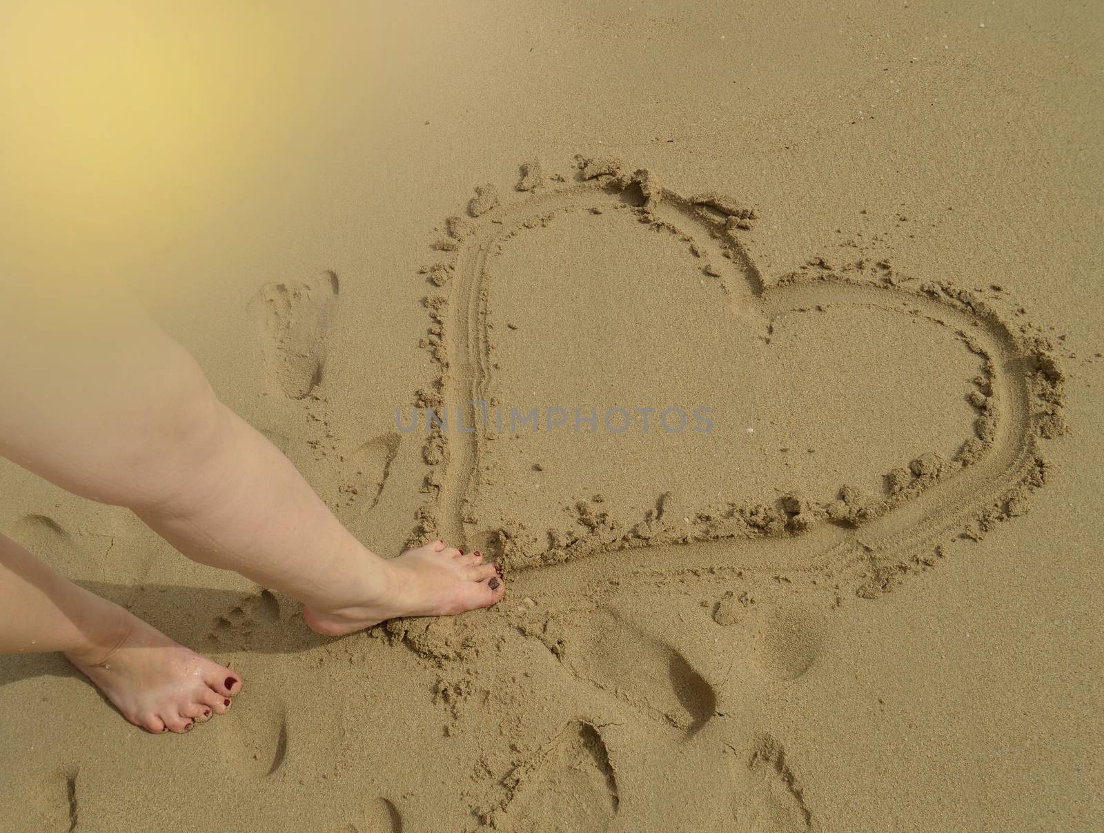 Hello summer, women's feet draw a heart sign on the wet sand while standing on the sandy beach. Concept of rest, relaxation, top view by claire_lucia