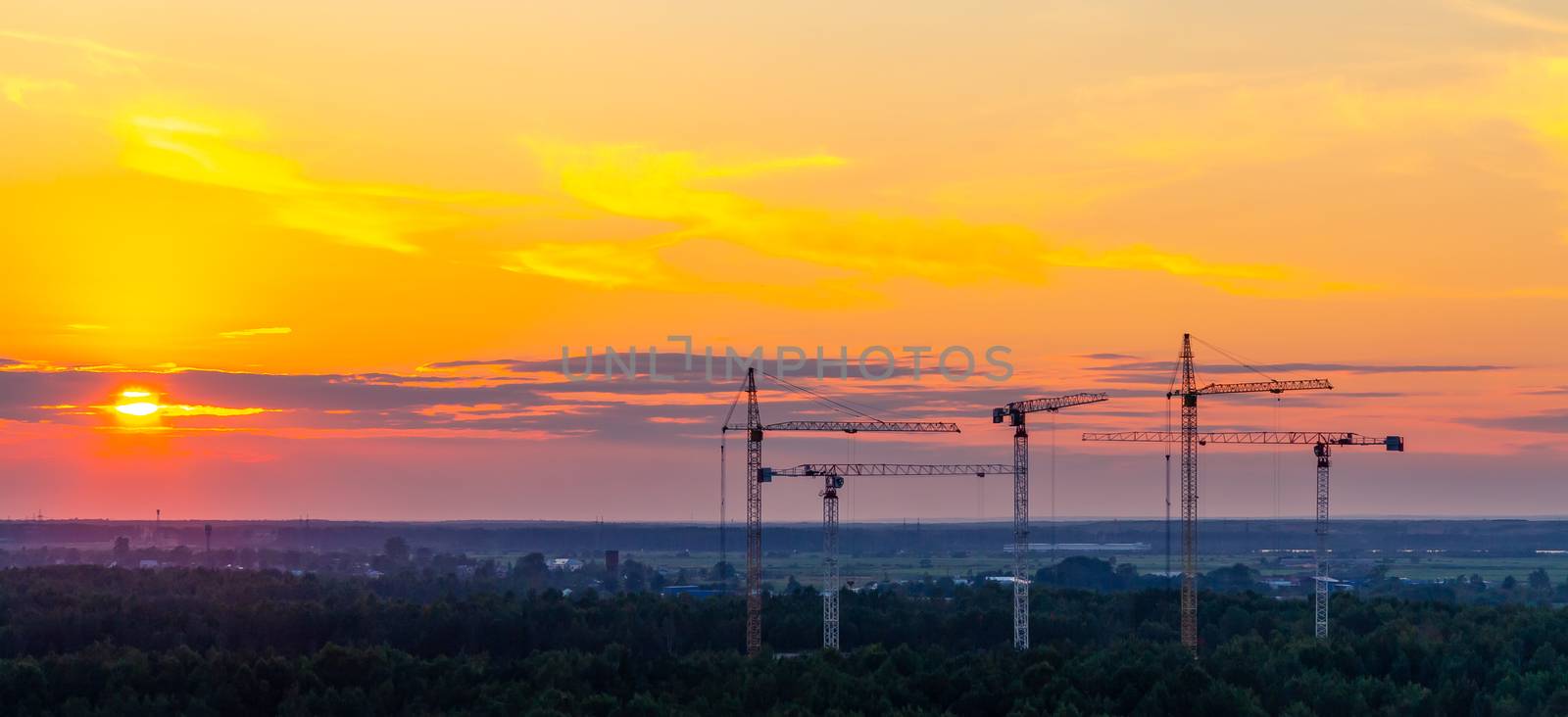 Several construction cranes on the background of colorful sunset sky by galsand