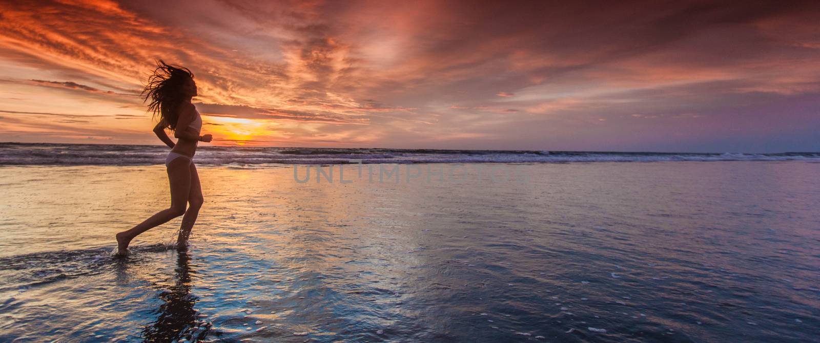 Beautiful sporty girl in bikini run on the seashore at sunset