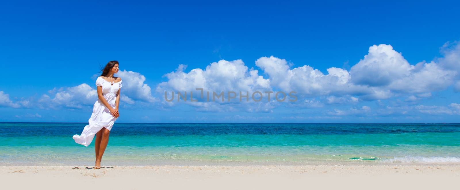 Woman in white dress walking in tropical sea beach enjoying wind