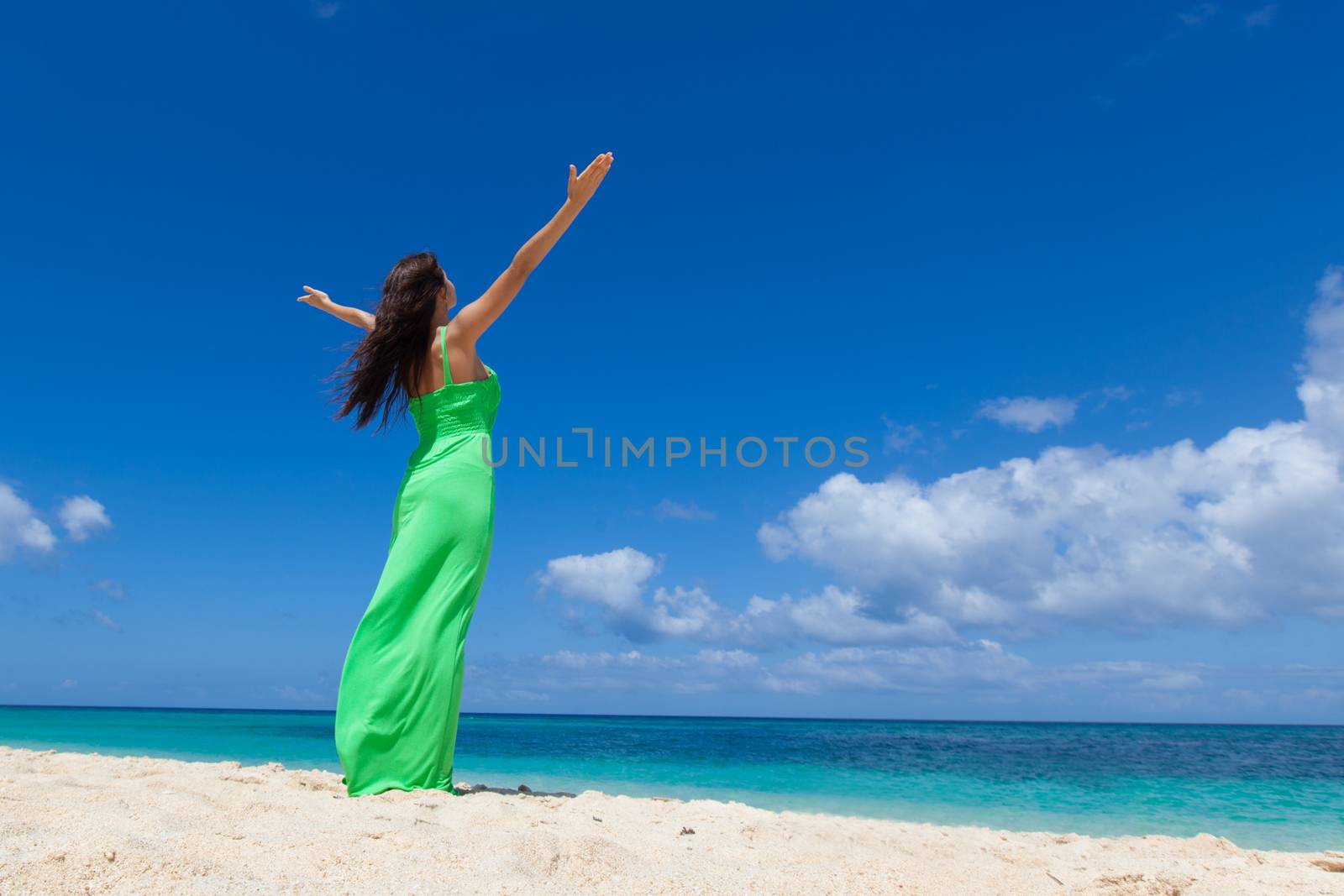 Woman in green dress posing in tropical sea beach with arms raised