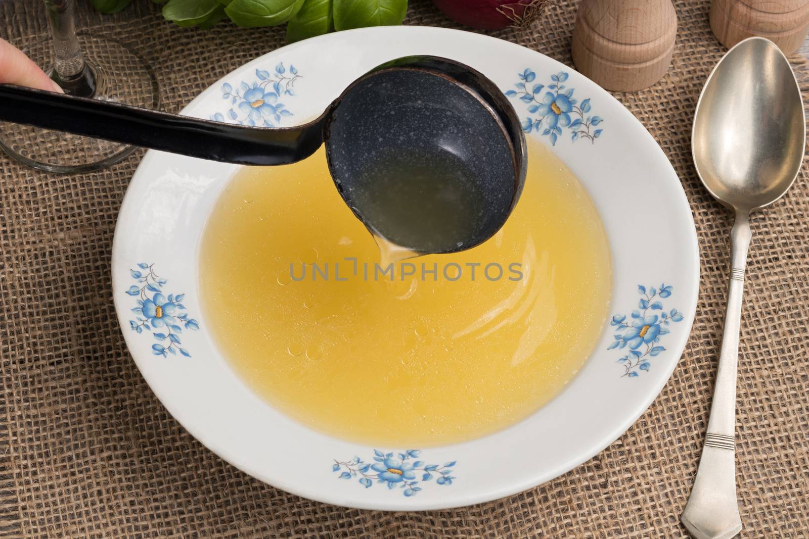 Pouring chicken bone broth into a soup plate with a ladle