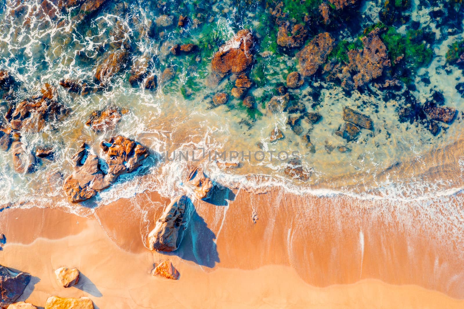 Rocky beach aerial viiews as waves wash in and out onto the shore